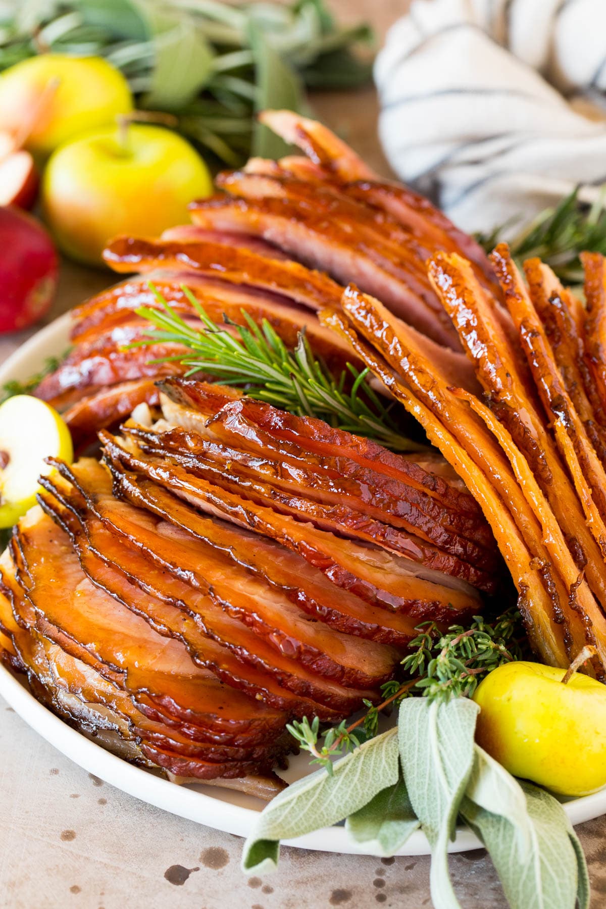 Sliced Easter ham on a plate garnished with herbs and apples.
