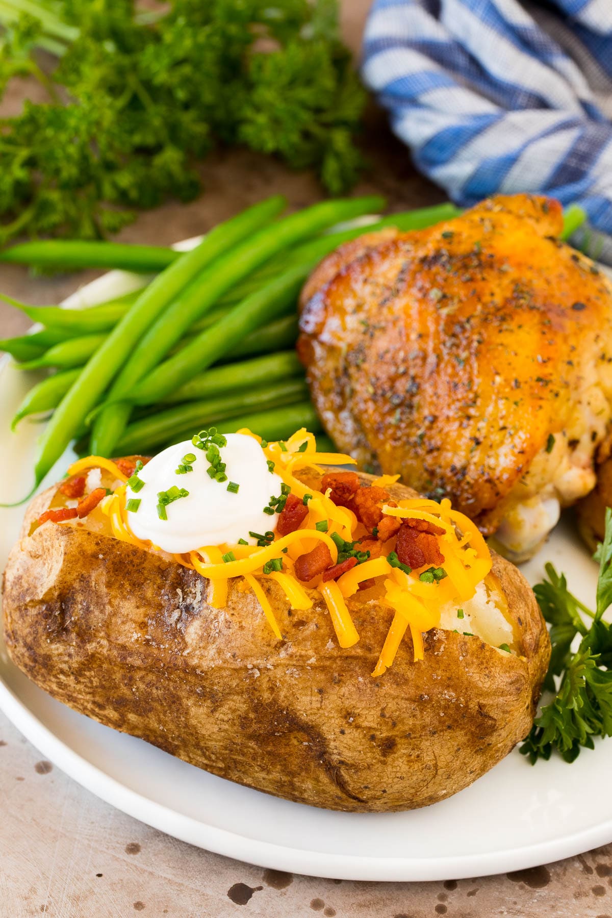 An oven baked potato served with chicken and green beans.
