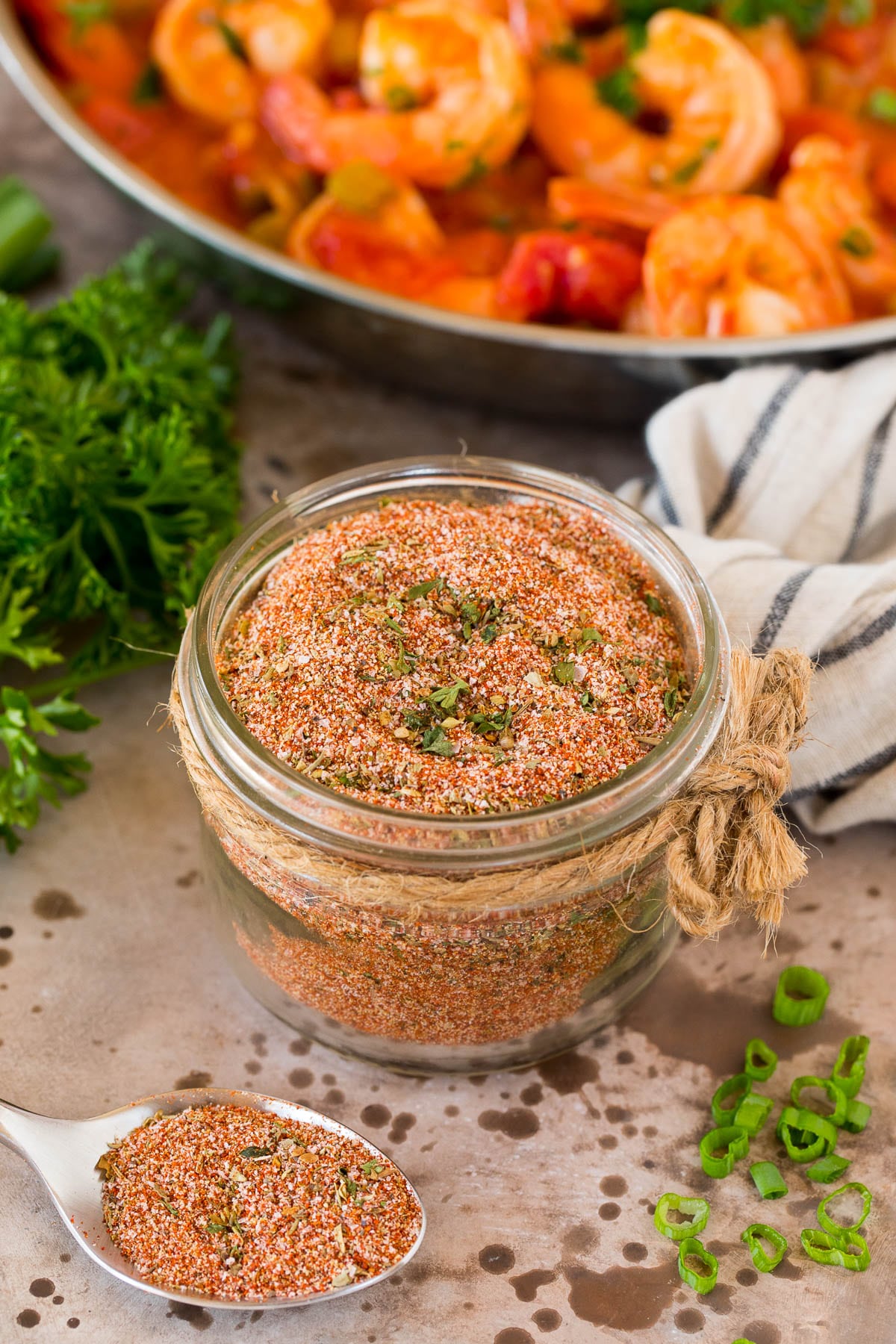 A jar of Creole seasoning surrounded by fresh herbs.