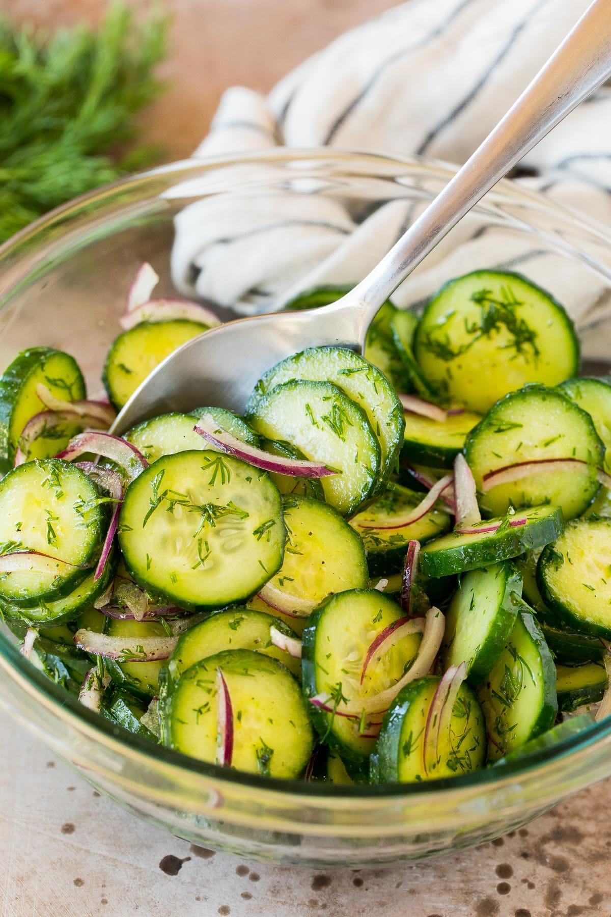 A bowl of cucumber dill salad with a spoon in it.