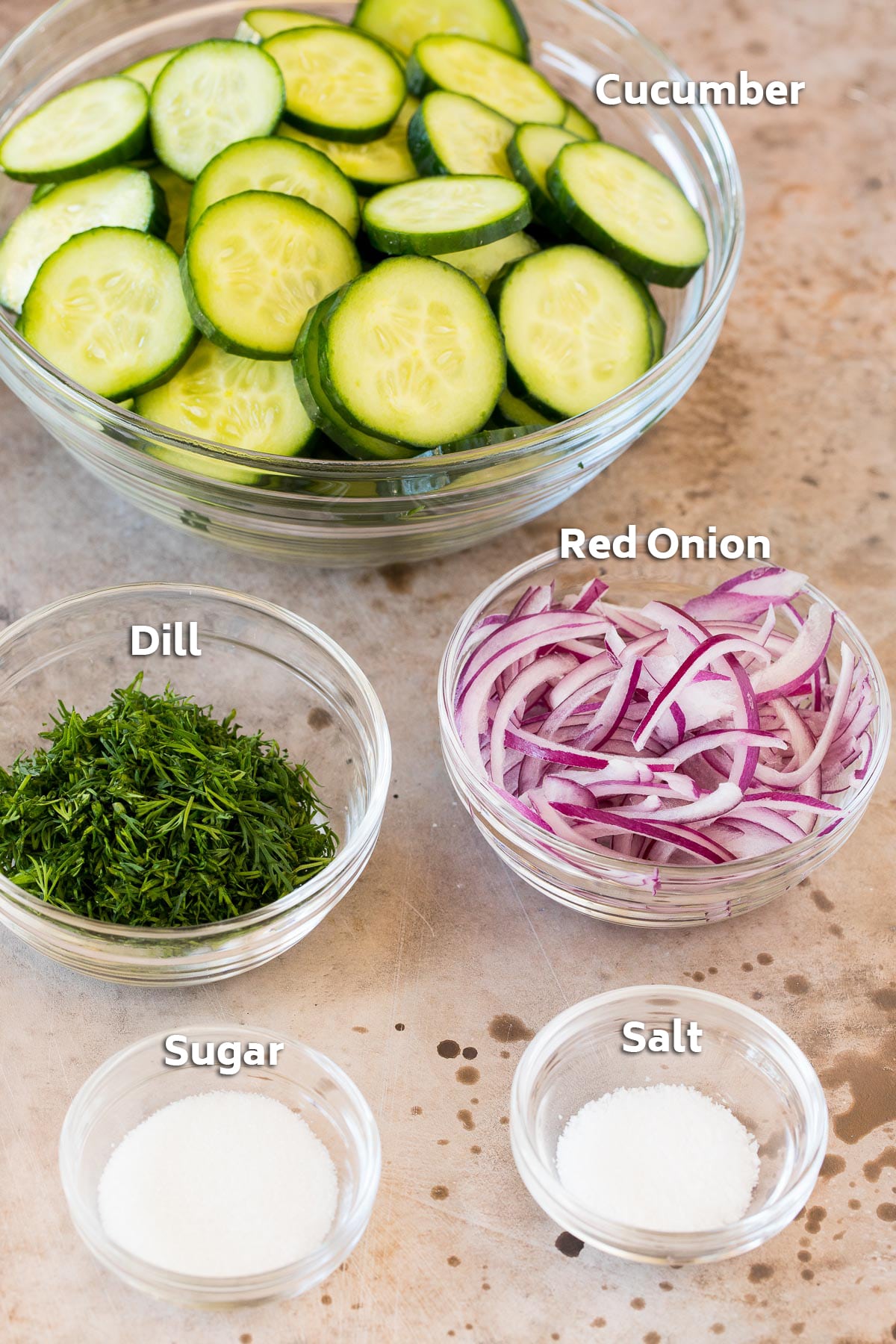 Bowls containing cucumbers, onion, dill, sugar and salt.