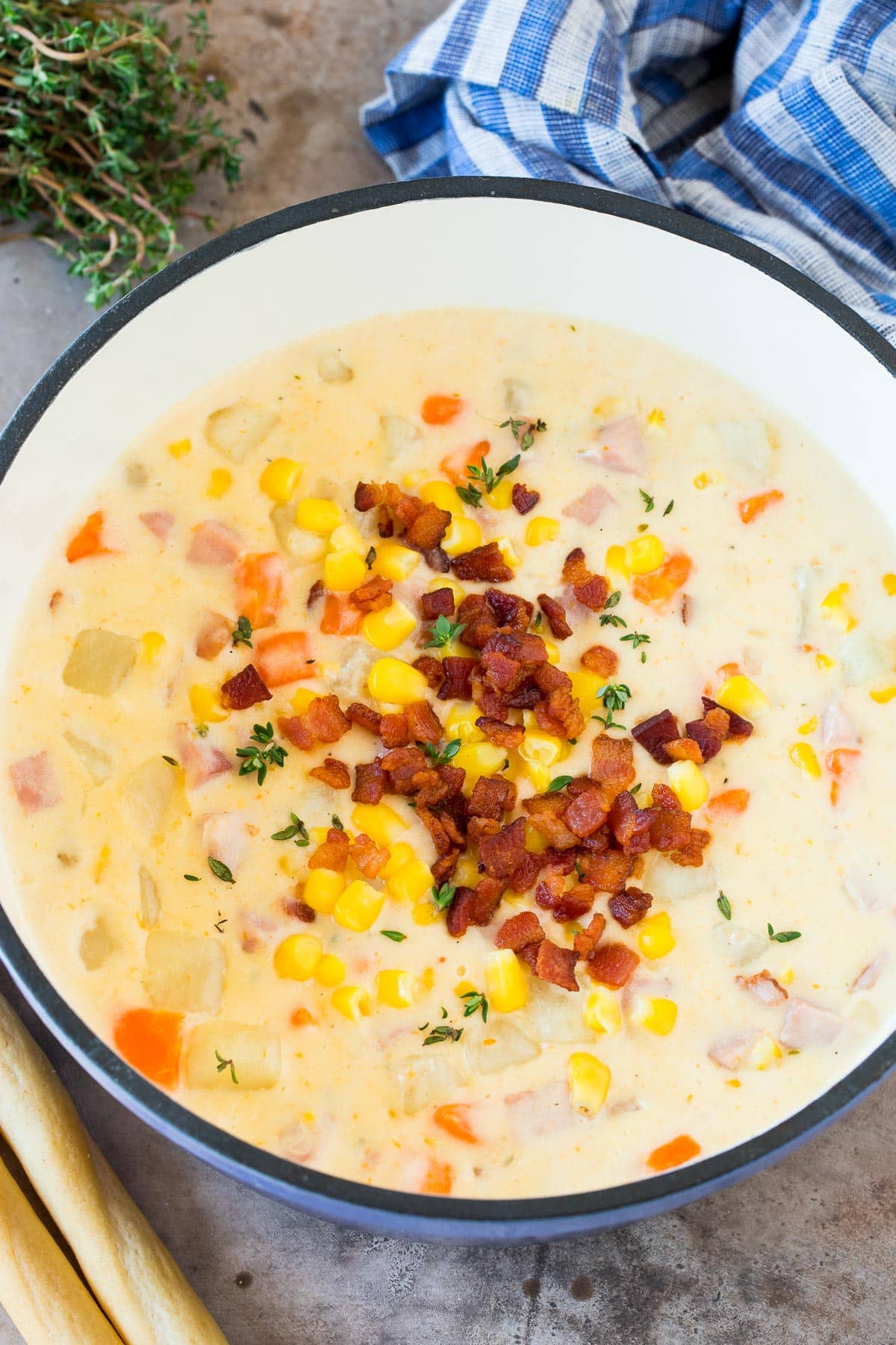 A pot of ham and corn chowder topped with bacon and corn.