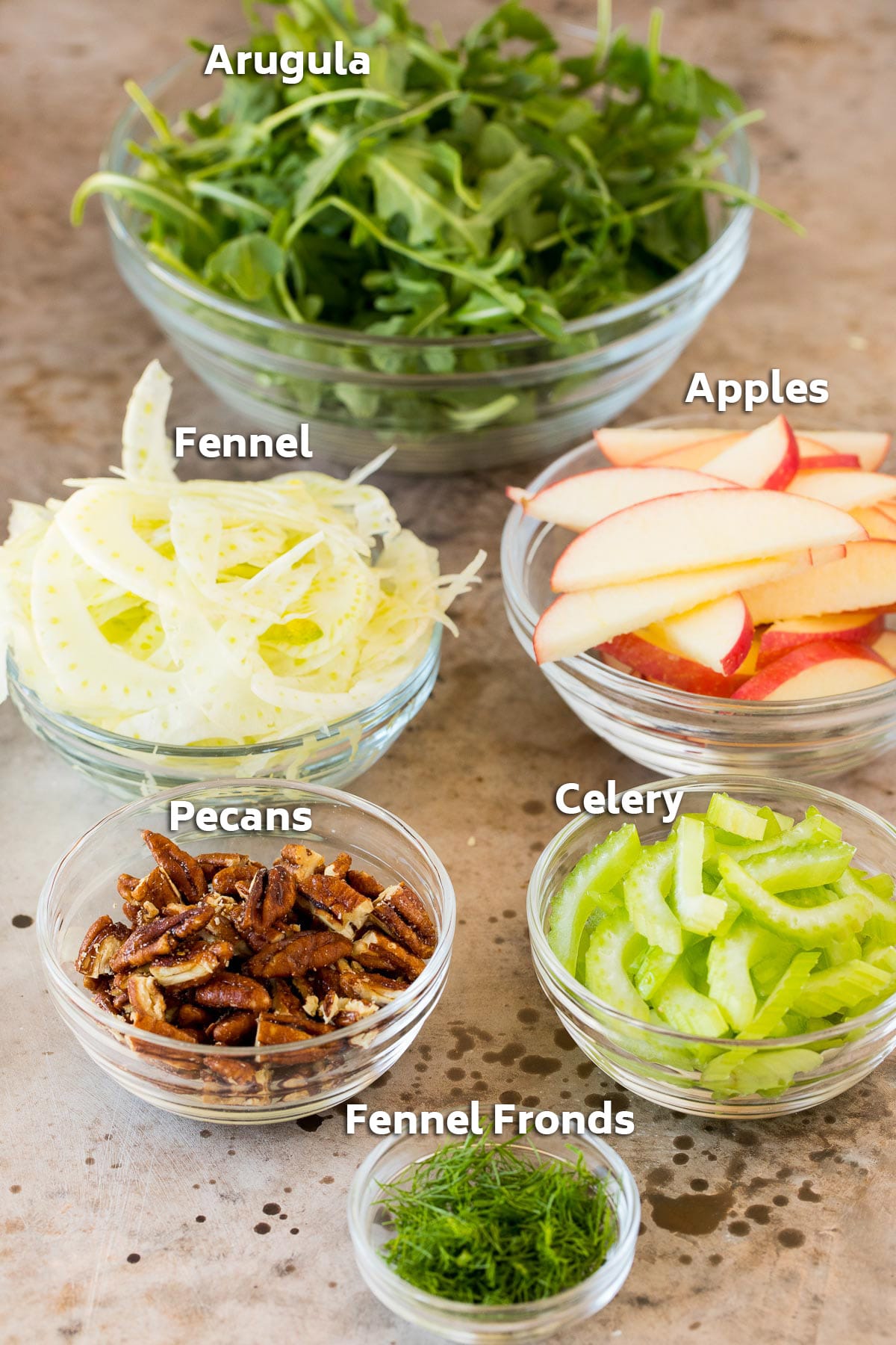 Bowls of ingredients including arugula, apples, fennel and pecans.