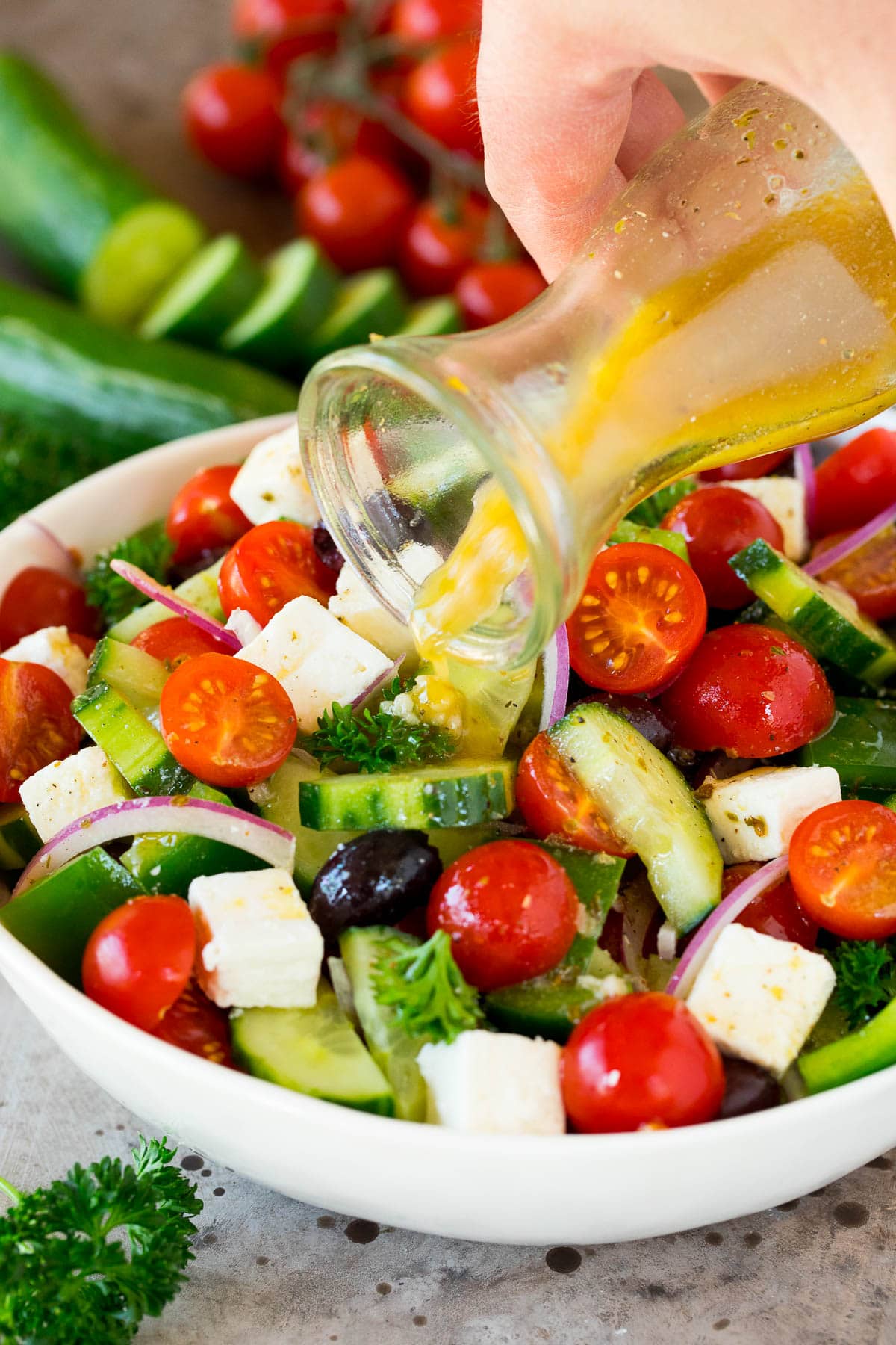 Greek salad dressing being poured over a bowl of diced vegetables.