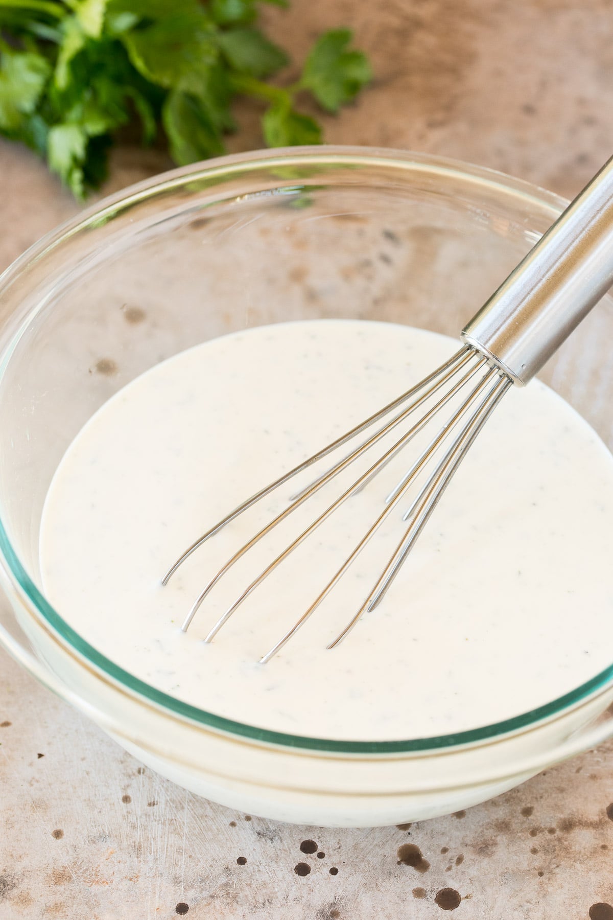 A bowl of creamy herb dressing with a whisk in it.