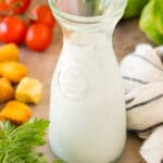 A glass container of homemade ranch dressing surrounded by salad ingredients.