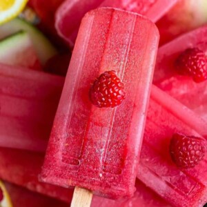An image of a watermelon popsicle with a raspberry on top.