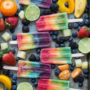 A picture of several rainbow colored popsicles with various fruit.