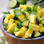 A picture of a salad made with pineapple and cucumber in a wooden bowl.