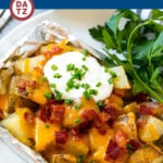 These grilled potatoes in foil are diced potatoes cooked in ranch butter, then topped with melted cheese, bacon, sour cream and chives.