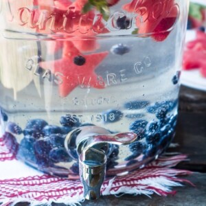 A picture of a jug of water with watermelon and berries in the water.