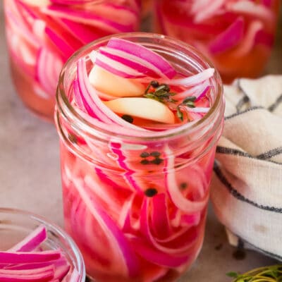 A jar of pickled red onions with garlic, pepper and thyme.