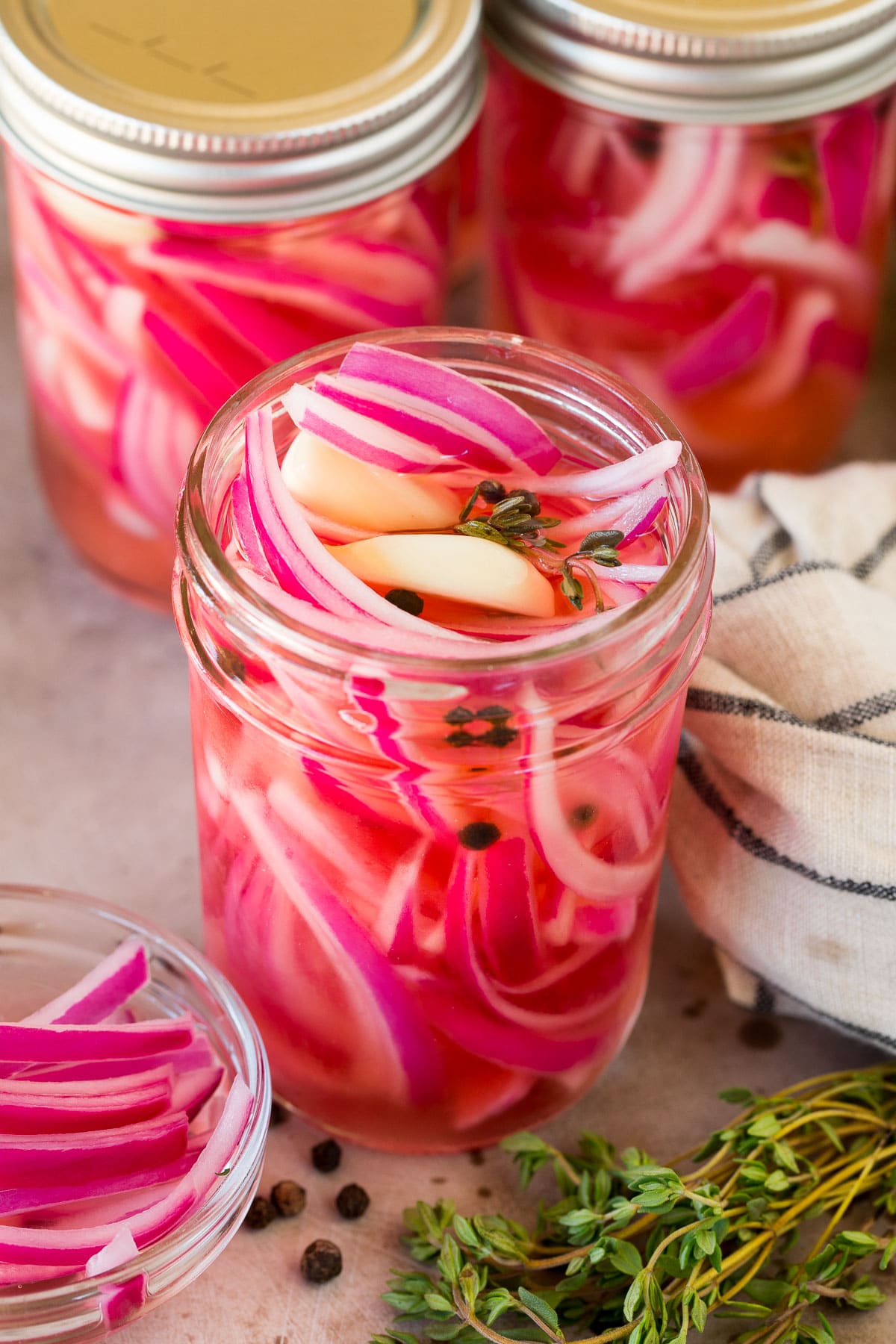 A jar of pickled red onions with garlic, pepper and thyme.