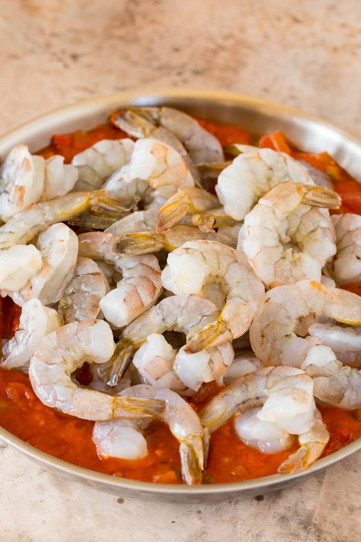 Raw shrimp in a pan of tomato sauce.