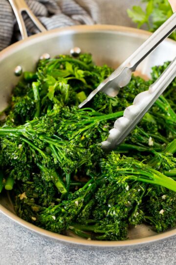 Tongs serving up a portion of sauteed broccolini.