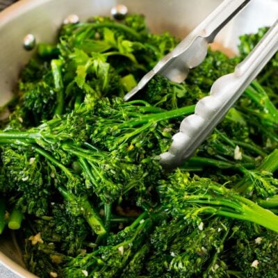 Tongs serving up a portion of sauteed broccolini.