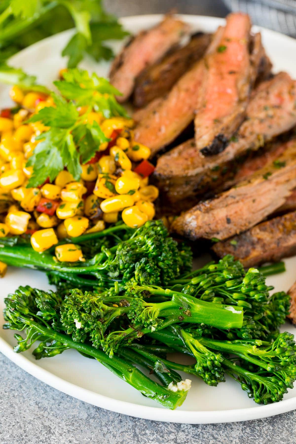 Cooked broccolini on a plate with steak and corn.