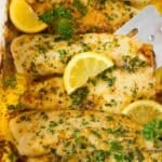 A spatula serving baked tilapia garnished with herbs and lemon.