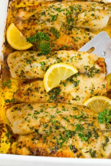 A spatula serving baked tilapia garnished with herbs and lemon.