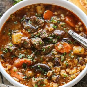 An image of a bowl of beef and barley soup with carrots.