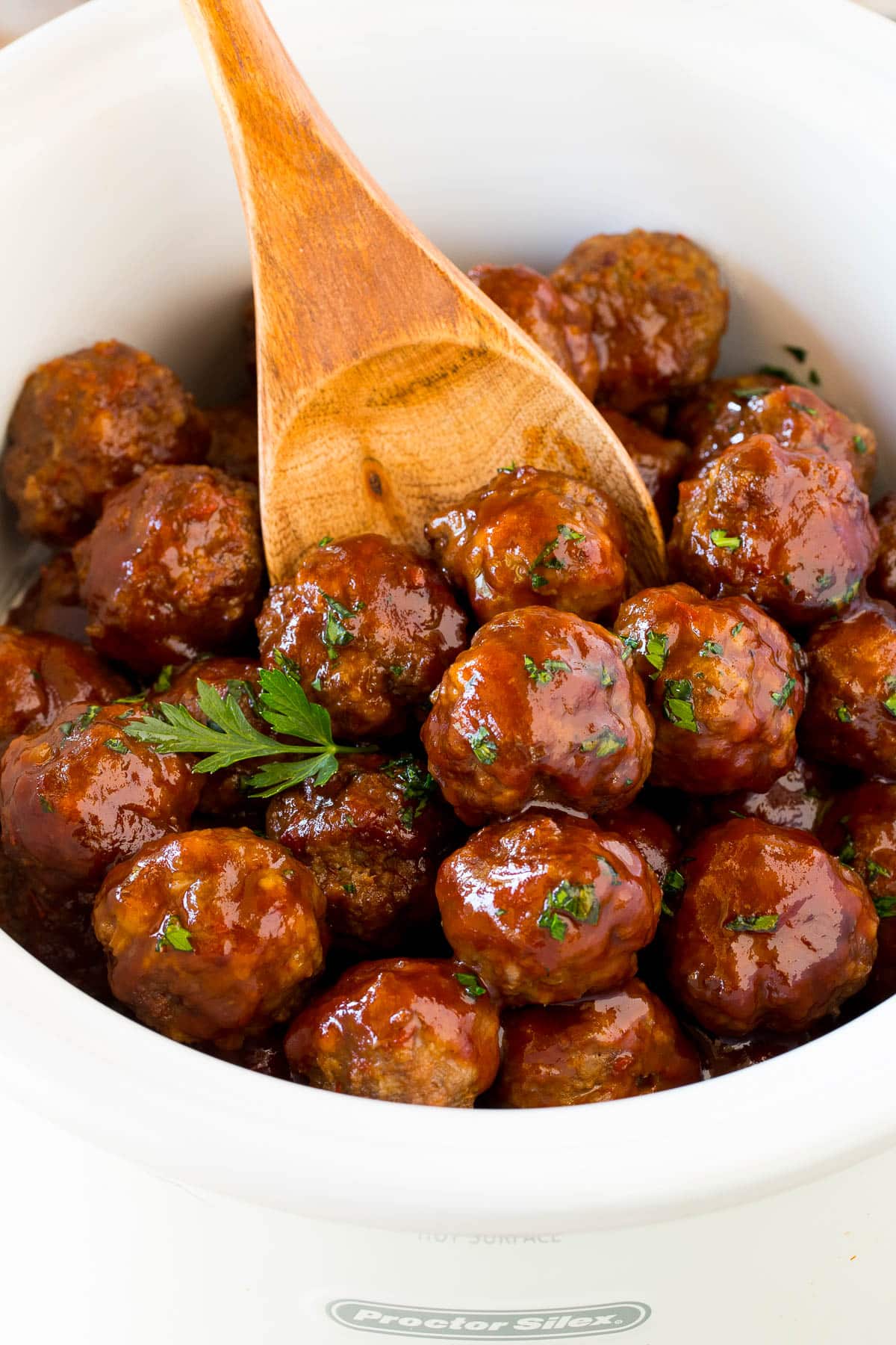 A slow cooker filled with grape jelly meatballs with a serving spoon in it.