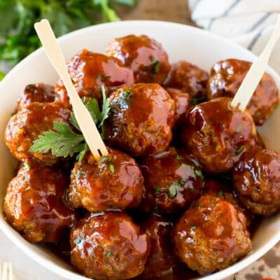A bowl of grape jelly meatballs served with cocktail forks.
