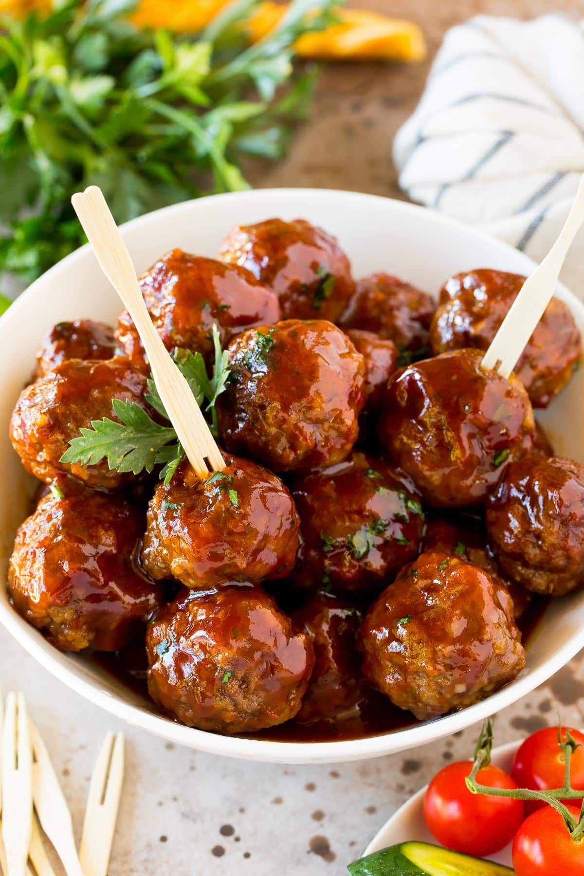 A bowl of grape jelly meatballs served with cocktail forks.