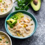 An image of a bowl of white chicken chili with avocado pieces on top.