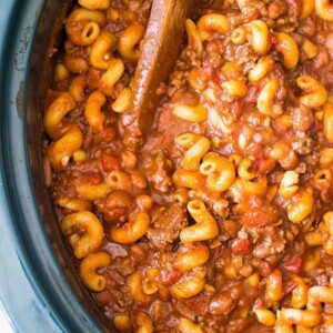 An image of chili mac in a slow cooker with a wood spoon.