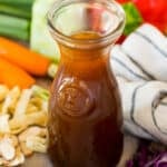 A jar of asian salad dressing surrounded by vegetables.