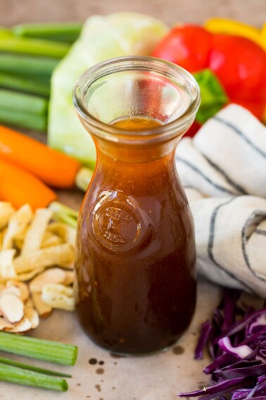 A jar of asian salad dressing surrounded by vegetables.