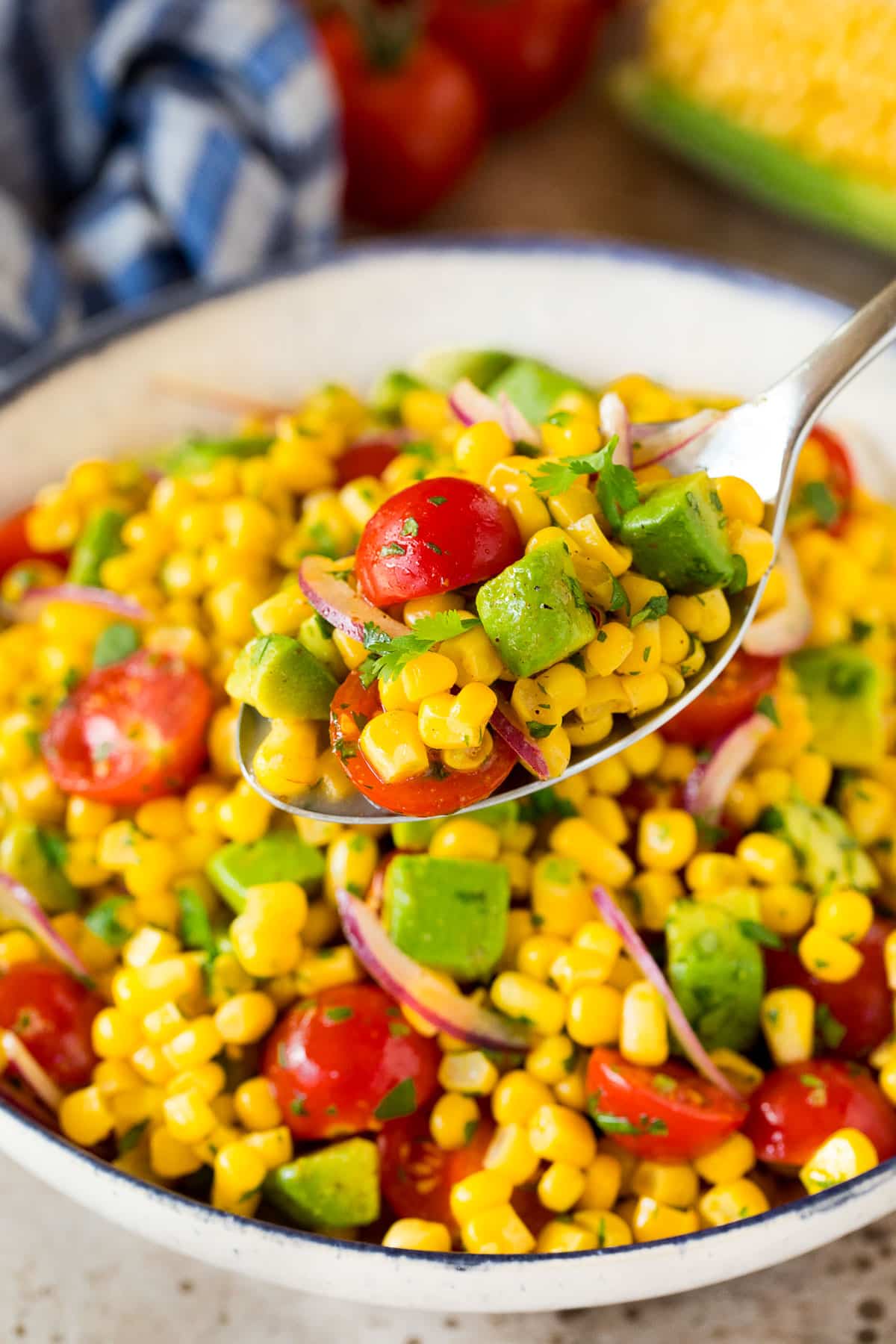 A spoon serving up a portion of salad made with avocado and corn.