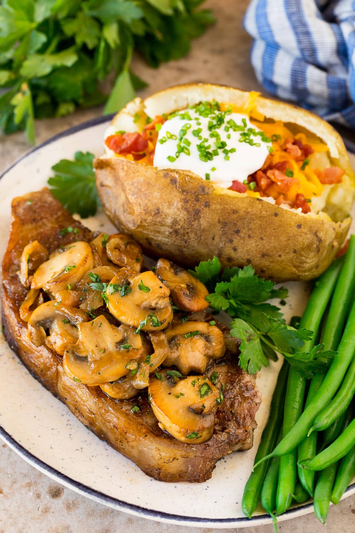 Sauteed mushrooms and onions on a steak with a baked potato on the plate.