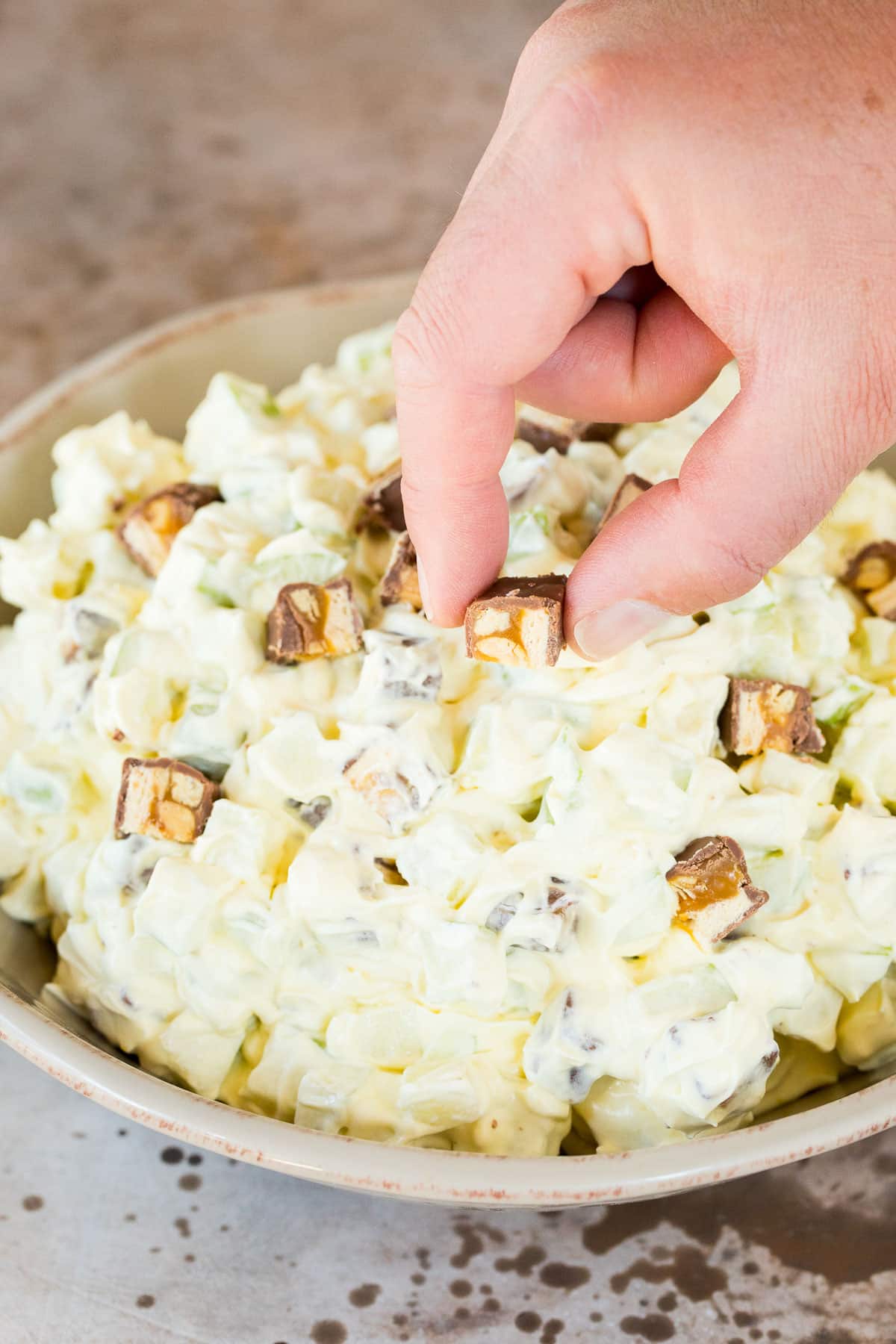 A hand placing chopped candy bars on apple salad.