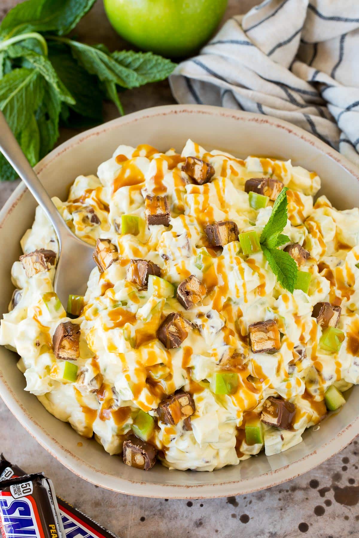 A bowl of snicker apple salad topped with caramel sauce.