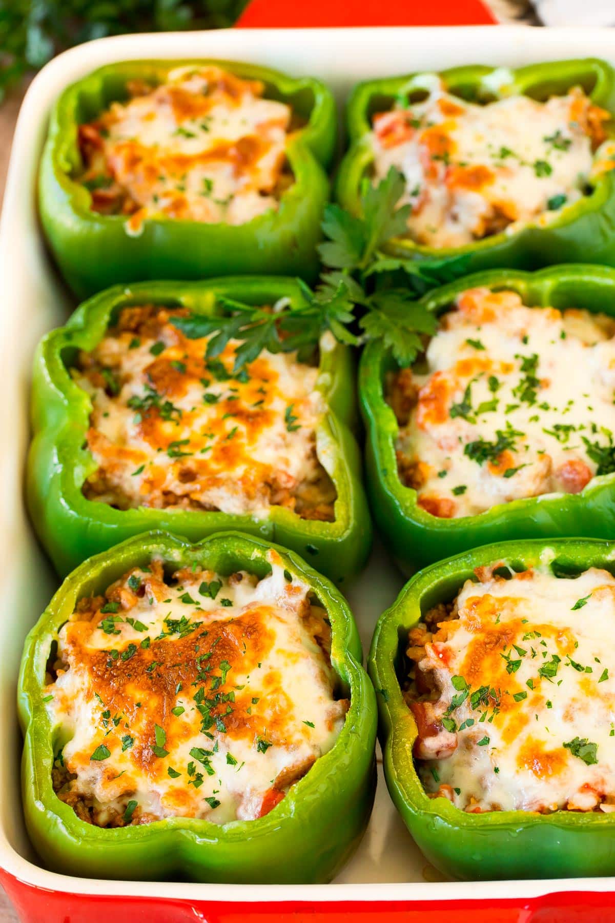 Stuffed green peppers topped with cheese in a baking dish.