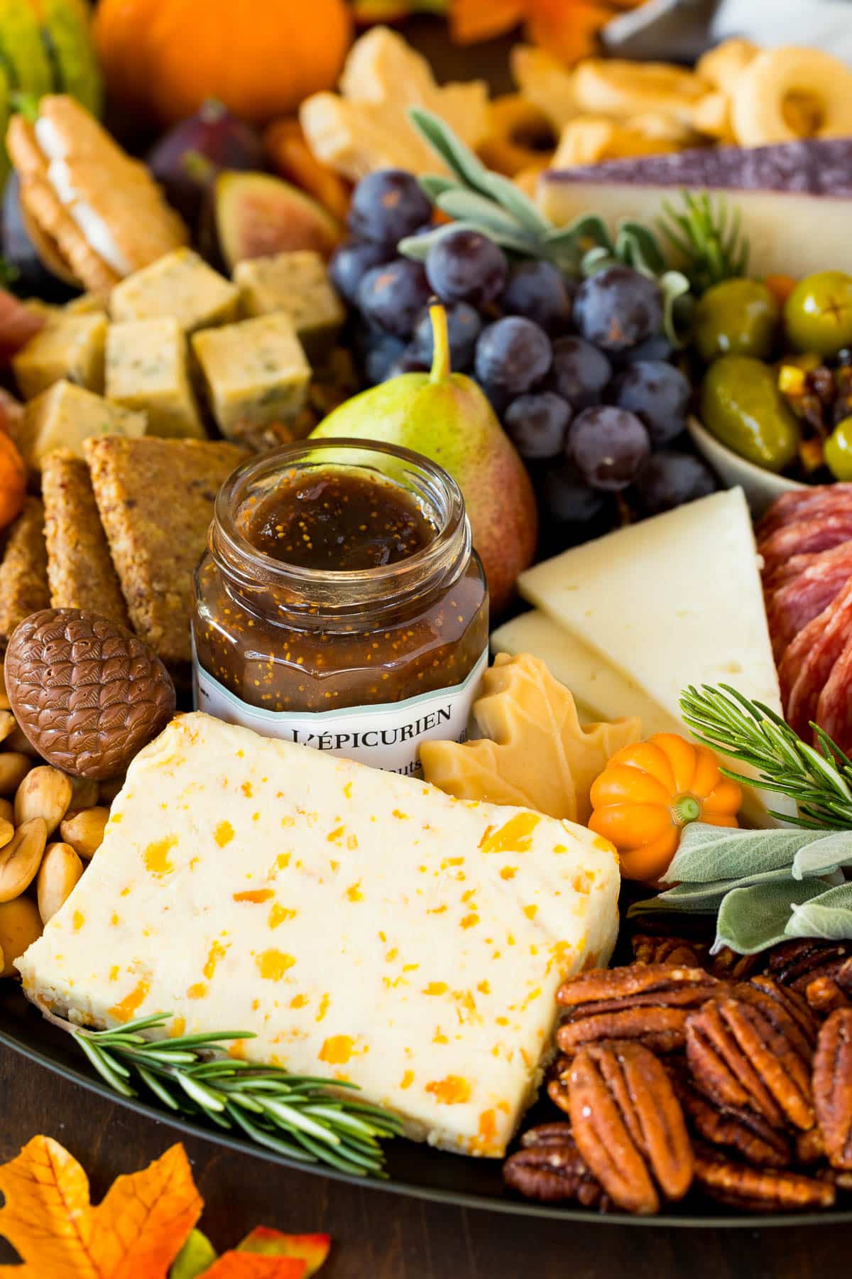 A close up of a meat and cheese board with nuts and a jar of jam.