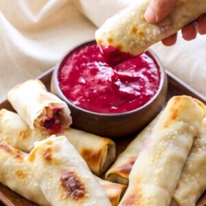 A picture of turkey, cranberry and brie eggrolls on a plate with one being dipped in sauce.