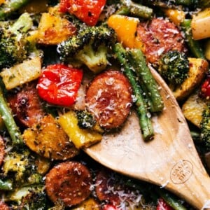 An image of a wooden spoon showing roasted veggies and sausage slices.