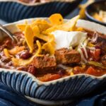 A picture of a bowl of slow cooker steak chili with sour cream and chips on top.