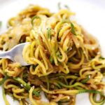 An image of stir fry zucchini noodles and onions on a forlk.