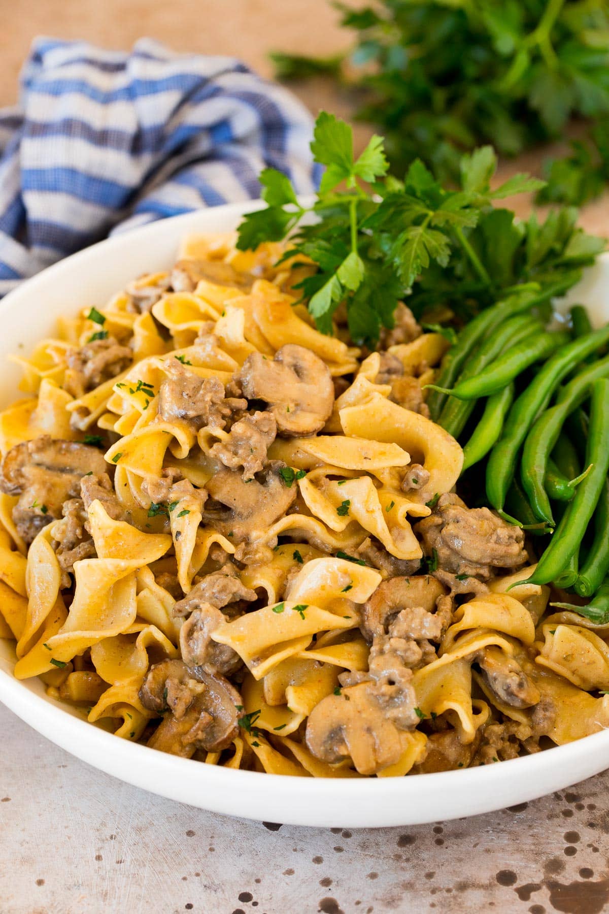 A serving bowl filled with ground beef stroganoff and a side of green beans.