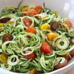 An image of a bowl of raw zucchini noodles with tomatoes and pesto.