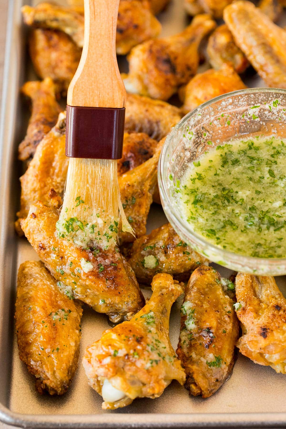 A brush coating chicken wings in garlic butter.