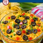 An image of a glass bowl of 7 layer dip surrounded by tortilla chips.