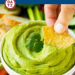 A bowl of avocado dip which is made with ripe avocados, cilantro, lime juice, jalapeno and sour cream, all blended together.