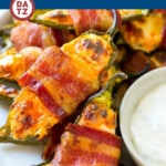 A plate of bacon wrapped jalapeno poppers loaded with cheese and wrapped with bacon.