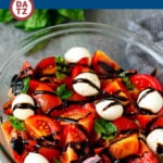 A bowl of caprese salad which is a blend of ripe tomatoes, fresh mozzarella, basil, olive oil and seasonings, all drizzled with balsamic glaze.