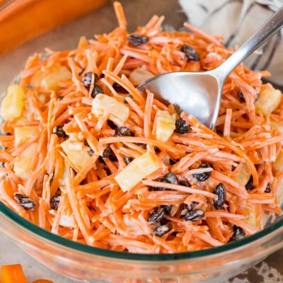 A bowl of creamy carrot salad with a large spoon in it.