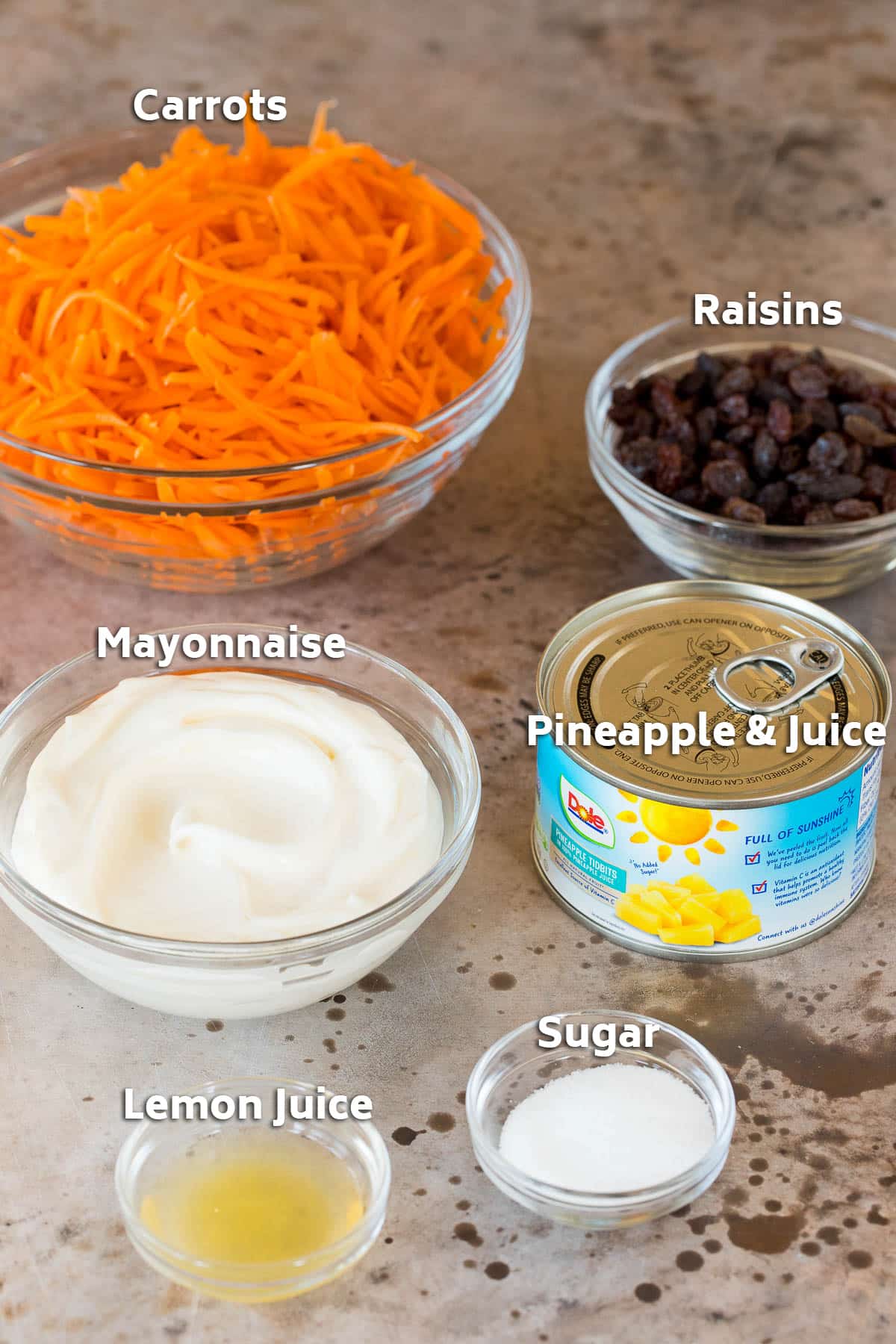 Bowls of ingredients including carrots, raisins, mayonnaise and seasonings.